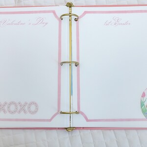 May include: A pink binder with two pages open. The left page has the text "1st Valentine's Day" and the text "XOXO" in pink. The right page has the text "1st Easter" and a drawing of a bunny in an egg.