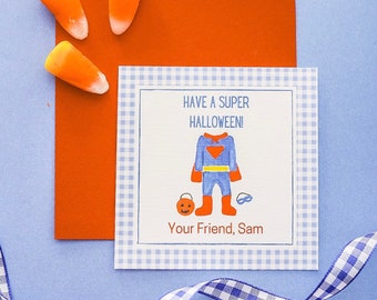 May include: A Halloween greeting card with a blue and white gingham border. The card features a superhero costume illustration and the text "HAVE A SUPER HALLOWEEN!" with the name "Sam." Candy corn and an orange envelope are also visible.