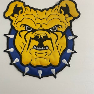 May include: Yellow embroidered bulldog patch with a blue collar and white spikes. The bulldog has a fierce expression with black eyes and a black nose.