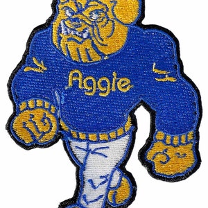May include: Embroidered patch featuring a stylized bulldog mascot in blue and gold. The bulldog is wearing a blue sweater with the word "Aggie" in gold lettering. The patch has a black border and is designed for application on clothing or accessories.