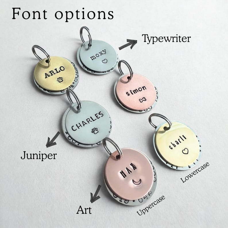 May include: Six circular metal pet ID tags in gold, silver, and copper tones, each featuring a split ring. The tags are engraved with names like ARLO, moxy, simon, CHARLES, charli, and MAX, alongside symbols including a paw print, heart, and bone.