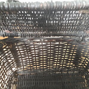 May include: Close-up of a black wicker basket, showcasing the intricate woven pattern. The basket's interior is visible, revealing the depth and texture of the weave. The basket appears to be vintage, with a focus on the craftsmanship.
