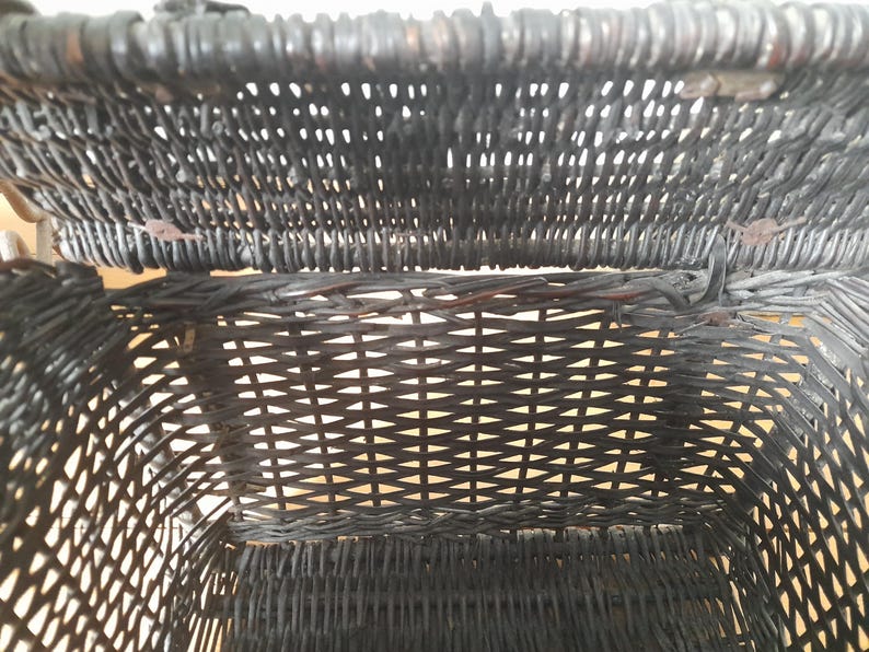 May include: Close-up of a black wicker basket, showcasing the intricate woven pattern. The basket's interior is visible, revealing the depth and texture of the weave. The basket appears to be vintage, with a focus on the craftsmanship.