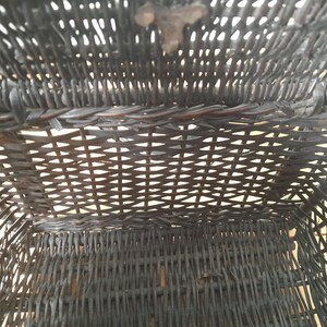 May include: An overhead view of a dark brown woven basket. The basket is rectangular with a woven pattern. The basket's interior is visible, showing the woven structure and the open space within. The basket appears to be made of natural materials.