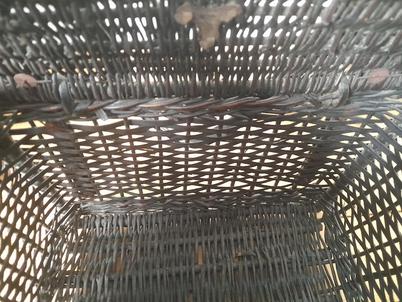 May include: An overhead view of a dark brown woven basket. The basket is rectangular with a woven pattern. The basket's interior is visible, showing the woven structure and the open space within. The basket appears to be made of natural materials.