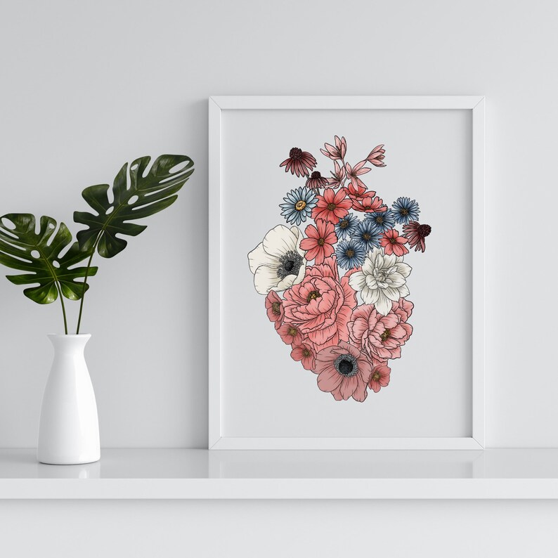 May include: A white framed print with a heart-shaped arrangement of pink, white, and blue flowers. The flowers are drawn in a realistic style.