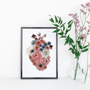 May include: A framed print of a heart-shaped floral arrangement. The flowers are pink, white, and blue, and they are arranged in a heart shape. The print is on a white background and has a black frame.