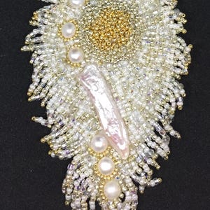 May include: A white and gold beaded necklace with a large pearl pendant. The pendant is surrounded by smaller pearls and gold beads. The necklace is a statement piece and would be perfect for a special occasion.