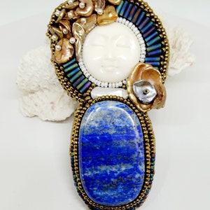 May include: A beaded pendant featuring a carved moon face, a lapis lazuli stone, and a cluster of iridescent and gold-toned beads.