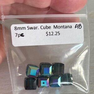 May include: A small plastic bag containing seven 8mm dark blue Swarovski cube beads with an iridescent finish. The bag has a label that reads "8mm Swar. Cube Montana AB 7pc $12.25".