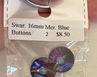 May include: Two 16mm Mer. Blue buttons in a clear plastic bag. The buttons are round with a faceted design, displaying shades of blue and purple. The label reads "Swar. 16mm Mer. Blue Buttons 2 $8.50".