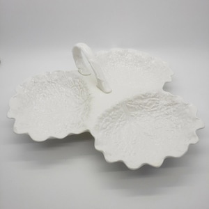 May include: White ceramic serving dish with three leaf-shaped compartments and a handle. The dish has a textured surface and a scalloped edge. Ideal for serving snacks or appetizers.