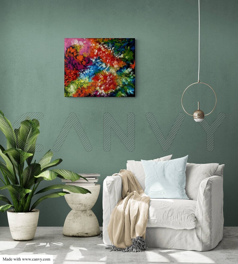 May include: Square abstract painting with a vibrant mix of colors including red, orange, blue, green, and pink. The artwork is displayed on a teal wall above a white armchair. A potted plant and side table are also visible.