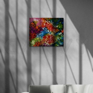 May include: Abstract art painting with a vibrant mix of colors including red, blue, green, and purple. The artwork is displayed on a wall above a sofa and a wooden table. The painting's texture and brushstrokes are visible.