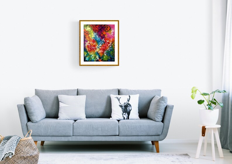 May include: A framed abstract art print with a gold frame. The artwork features a vibrant mix of colors, including red, yellow, blue, and green, creating a dynamic floral or landscape-inspired composition. The print is displayed above a gray sofa.