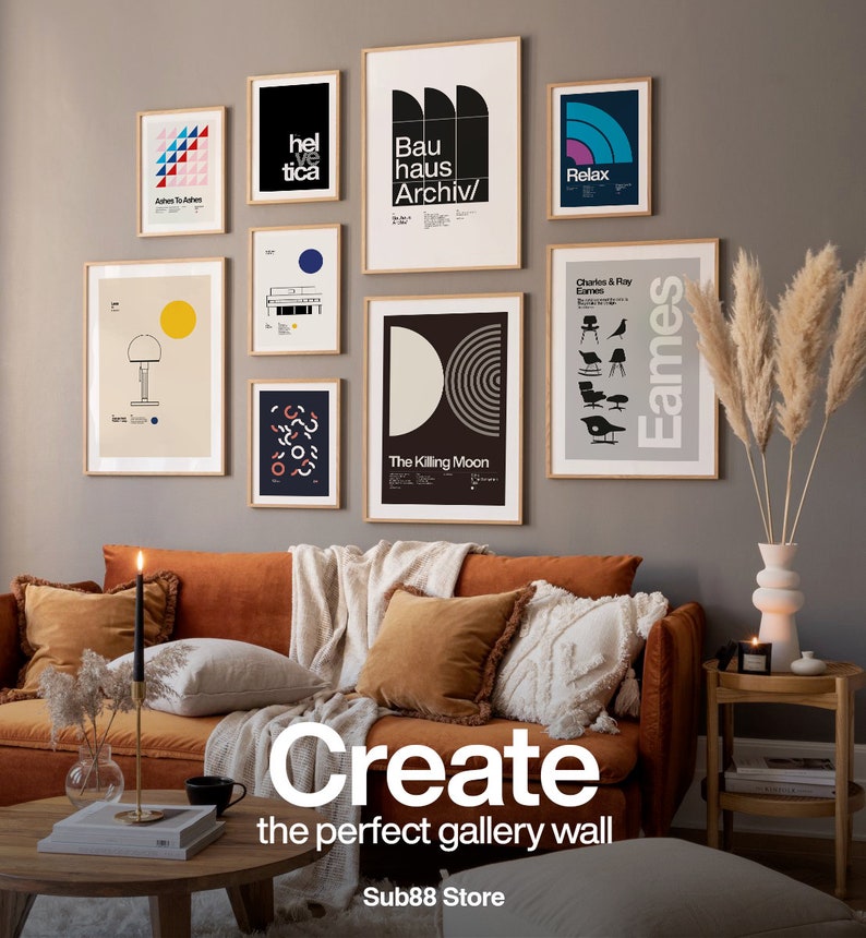 May include: A living room interior design featuring a brown velvet sofa with pillows and a throw blanket. The wall behind the sofa is decorated with a gallery wall of framed prints with geometric designs and text, including "Bauhaus Archiv", "Helvetica", "The Killing Moon", "Relax", and "Charles & Ray Eames". A vase with dried pampas grass is on a side table.