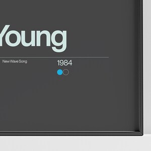 May include: A framed print with the word "young" in a light blue font. The text "New Wave Song" is below the word "young" and the year "1984" is below that. There are two small circles to the right of the year, one blue and one gray.