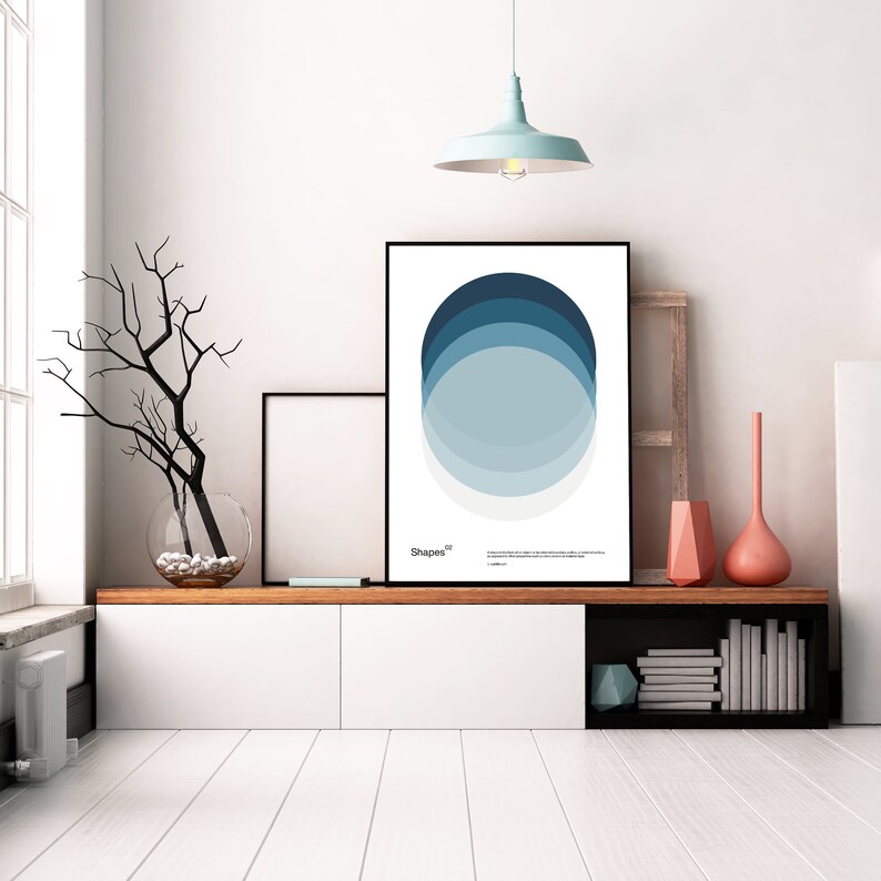 May include: A framed print with a minimalist design featuring overlapping circles in shades of blue. The print is titled "Shapes" and is displayed on a white wall above a wooden shelf with a vase of branches and a framed picture.