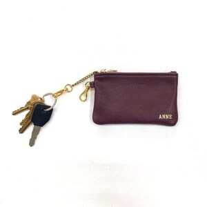 May include: A burgundy leather key chain with a gold chain and a small zippered pouch. The pouch has the word "ANNE" embossed on it.