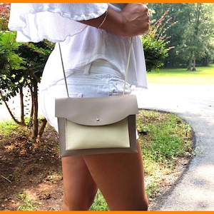 May include: A small beige and cream leather crossbody bag with a flap closure and a single pocket on the front.