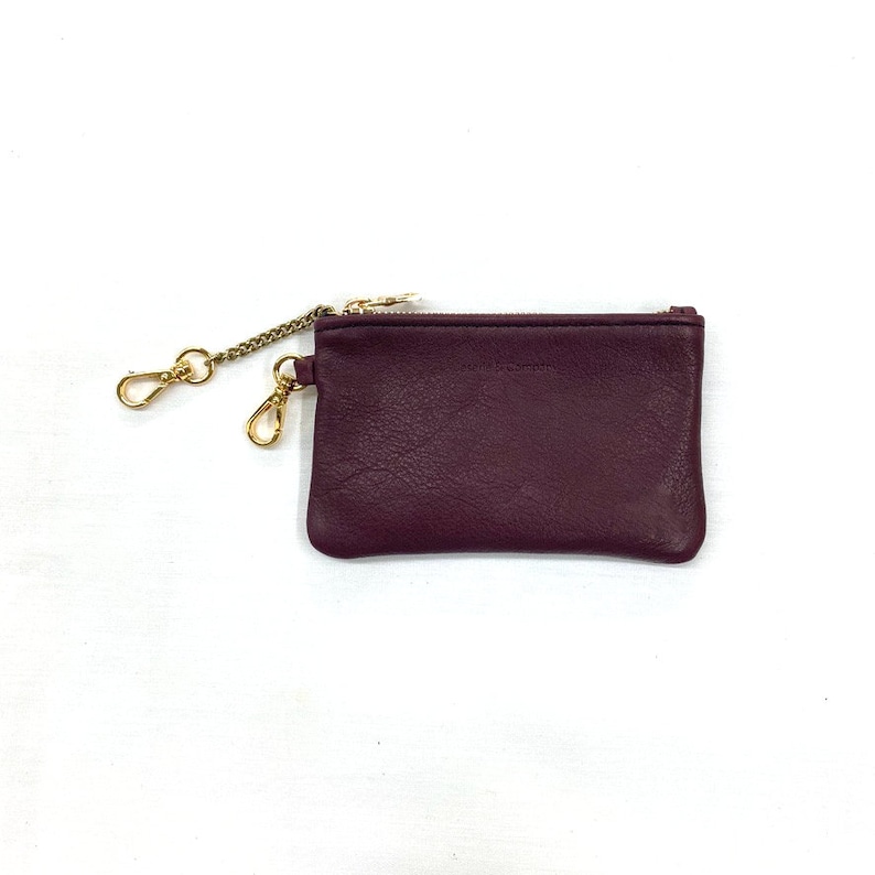 May include: A small, burgundy leather coin purse with a gold zipper and a gold chain attached.