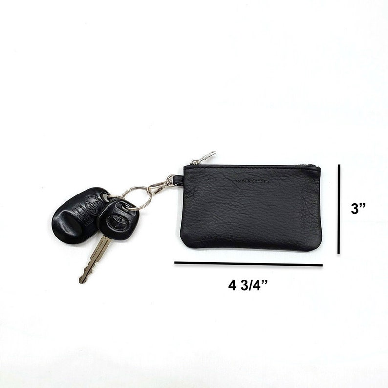 May include: Black leather key chain with a zipper closure. The keychain is 4 3/4 inches wide and 3 inches tall. It has a silver key ring with two car keys attached.