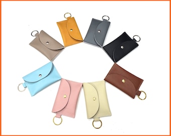 May include: Assortment of ten keychains in various colors, including brown, gray, black, blue, pink, and cream. Each keychain features a small, rounded pocket with a gold metal ring.