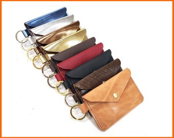 May include: A set of eight leather keychains in various colors, including blue, silver, gold, brown, red, black, brown with a snakeskin pattern, and tan. Each keychain has a metal ring attached.