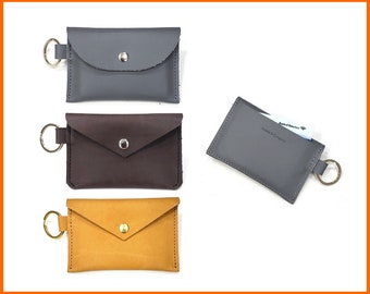 May include: Three leather keychains with a snap closure. The keychains are in gray, brown, and yellow. The gray keychain has a card slot and a Bank of America card is inserted in the slot. The text on the card reads "Bank of America" and "Jassby & Company".