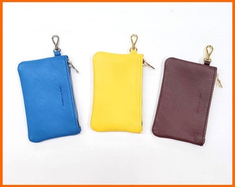 Puede incluir: Tres pequeñas bolsas de cuero con cremallera y anillas. Las bolsas son azules, amarillas y burdeos.