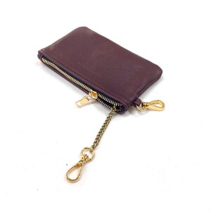 May include: A burgundy leather zippered pouch with a gold chain and clasp. The pouch is lying on a white surface.