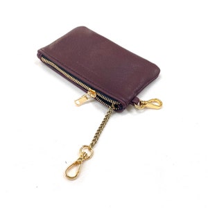 May include: A burgundy leather zippered pouch with a gold chain and clasp. The pouch is small and compact, perfect for carrying keys or other small items.