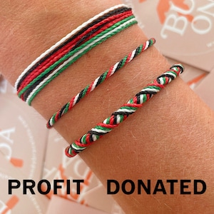 以下が含まれることがあります： 赤、黒、白、緑の3色の織りブレスレットが手首に表示されています。ブレスレットは編み紐で作られています。「PROFIT DONATED」というテキストが画像の下部にあります。