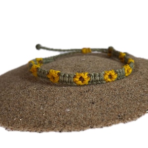 May include: A green and yellow friendship bracelet with a sunflower design. The bracelet is made of string and is tied in a knot.