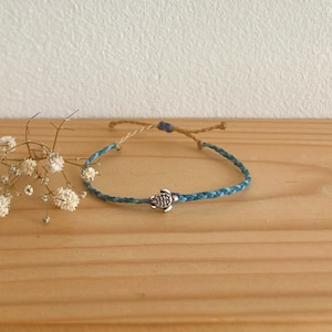 Op de afbeelding: Een gevlochten armband in blauw en groen met een zilveren schildpadbedel.