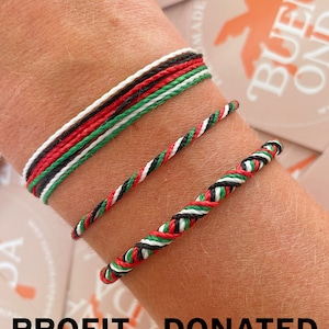 Puede incluir: Tres pulseras hechas de cordón trenzado en rojo, blanco, negro y verde. La pulsera superior presenta múltiples hilos paralelos, la del medio es un cordón fino trenzado y la inferior es una trenza más gruesa. El texto PROFIT DONATED es visible.
