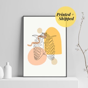 Peut inclure: Une impression minimaliste d'art en ligne d'une cage thoracique avec des formes abstraites en pêche, jaune et marron. L'impression est encadrée et exposée sur une étagère blanche.