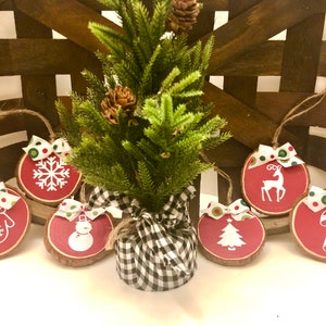 May include: Six red and white wooden Christmas ornaments with various holiday designs, including a snowflake, mitten, snowman, reindeer, Christmas tree, and candy cane. The ornaments are decorated with green and red polka dot ribbon.