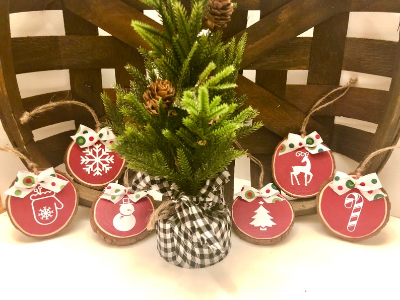 May include: Six red and white wooden Christmas ornaments with various holiday designs, including a snowflake, mitten, snowman, reindeer, Christmas tree, and candy cane. The ornaments are decorated with green and red polka dot ribbon.