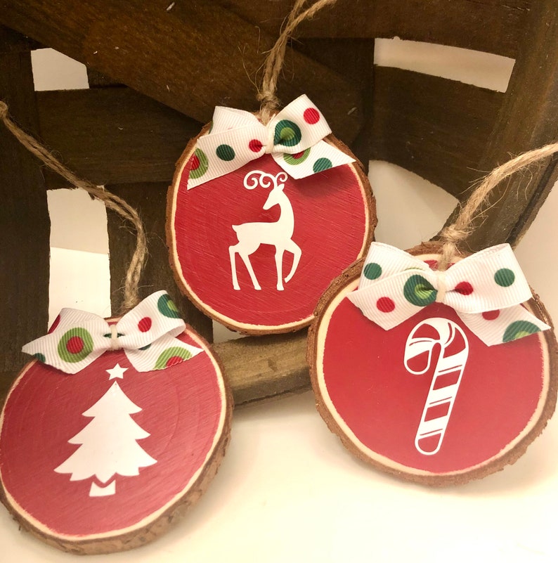 May include: Three red wooden ornaments with white designs and green and red polka dot bows. The designs are a reindeer, a Christmas tree, and a candy cane.