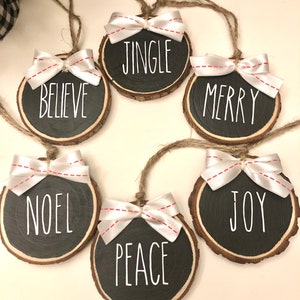 May include: Six round wood slice ornaments with white ribbon bows and black painted text. The ornaments read "Jingle", "Believe", "Merry", "Noel", "Joy", and "Peace".