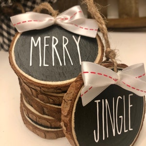May include: Two round wood slice ornaments with black paint and white lettering. One ornament says "Merry" and the other says "Jingle". Both ornaments have white ribbon bows with red stitching.