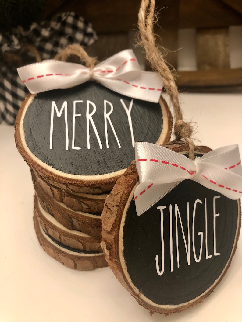 May include: Two round wood slice ornaments with black paint and white lettering. One ornament says "Merry" and the other says "Jingle". Both ornaments have white ribbon bows with red stitching.