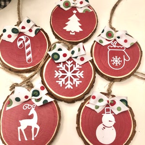 May include: Six red wooden ornaments with white Christmas designs and green and red polka dot bows. The designs include a Christmas tree, a candy cane, a snowflake, a mitten, a reindeer, and a snowman.