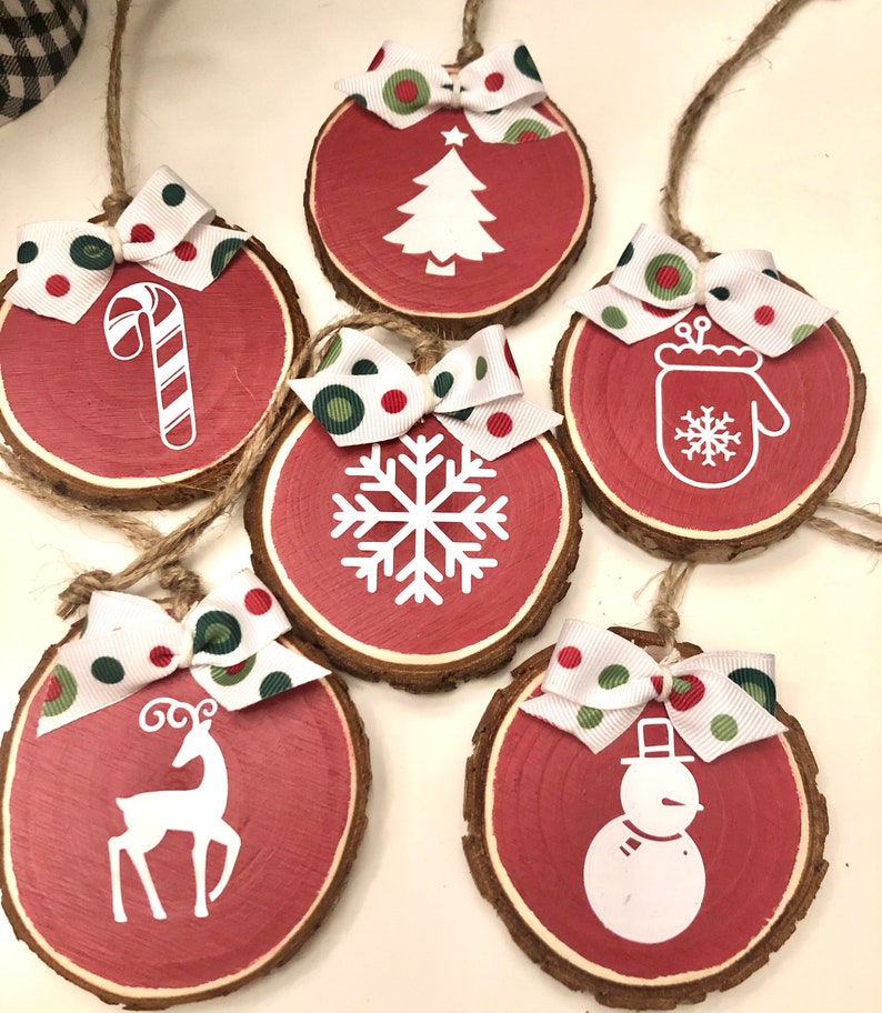 May include: Six red wooden ornaments with white Christmas designs and green and red polka dot bows. The designs include a Christmas tree, a candy cane, a snowflake, a mitten, a reindeer, and a snowman.