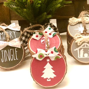 May include: Set of six wood slice Christmas ornaments with various designs. The ornaments are painted in red, gray, and black with white designs. The designs include a Christmas tree, a candy cane, a star, a nativity scene, and the words "Merry Jingle".