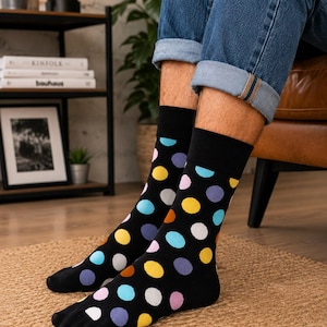 May include: A pair of black crew socks featuring a vibrant, multi-colored polka dot pattern. The dots are arranged in various colors including yellow, light blue, lavender, white, and orange, set against a solid black background with black cuffs.