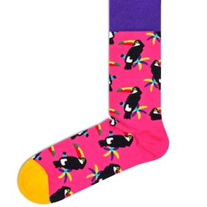 Peut inclure: Une chaussette rose avec un motif de toucans noirs, de palmiers colorés et un bout jaune. Le bord-côte est violet. Les toucans ont des becs jaunes et sont perchés sur des palmiers colorés.