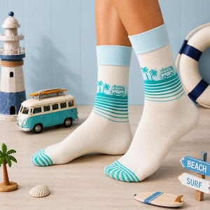 Könnte beinhalten: Cremeweiße Socken mit hellblauem Rippbündchen und türkisfarbenem Grafikdruck. Das Design zeigt ein horizontales Muster aus Palmen, einem Vintage-Campingbus und parallelen Linien sowie ein türkisfarbenes Streifenmuster im Zehenbereich.