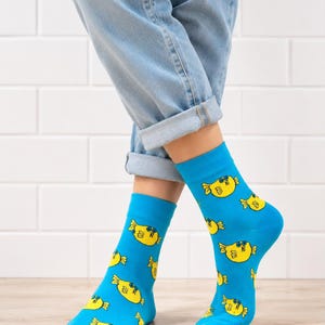 Könnte beinhalten: Ein Paar leuchtend blaue Socken mit einem wiederkehrenden Muster aus kleinen, gelben, runden Fischfiguren mit blauen Augen und Flossen. Die Socken werden zu einer hellblauen Jeans mit umgeschlagenen Säumen getragen, die bis zur Wadenmitte reicht.